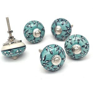 Peut inclure: Ensemble de quatre boutons de cabinet en céramique bleu sarcelle avec un motif floral blanc et noir. Chaque bouton a une base en métal argenté.