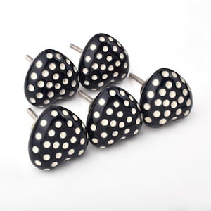 May include: A set of six black ceramic cabinet knobs with a white polka dot pattern. Each knob is heart-shaped and has a silver screw for easy installation. These decorative knobs are perfect for adding a touch of whimsy to furniture.