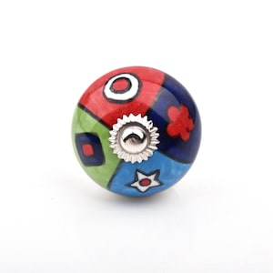 Peut inclure: Bouton de meuble en céramique colorée avec une base en métal argenté. Le bouton est divisé en sections rouges, vertes, bleues et blanches, chacune avec un design unique. Le bouton est rond et a une finition brillante.