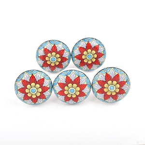 May include: Five round ceramic cabinet knobs with a floral design. Each knob features a red flower with yellow and blue accents, set against a light blue background with a white pattern. The knobs are arranged on a white surface.