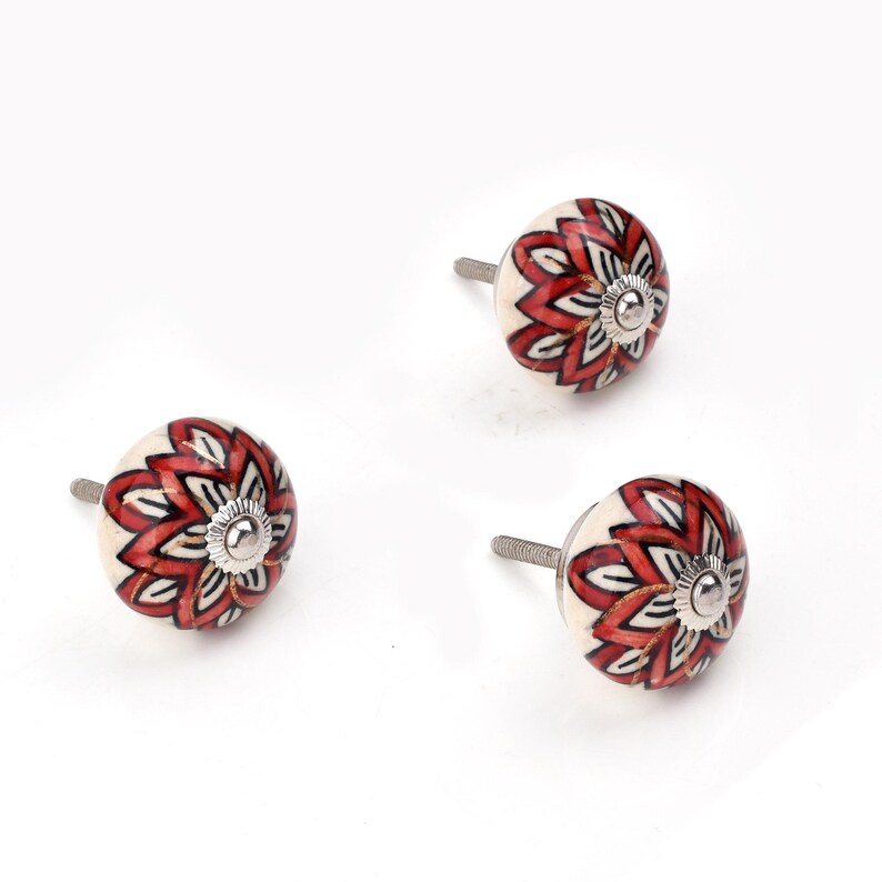 Red ceramic knobs with hand-painted white floral and mandala designs; assorted cabinet knobs for furniture and home décor.