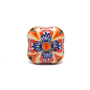 Könnte beinhalten: Ein quadratischer Keramik-Schrankknauf mit einem farbenfrohen Blumendesign. Der Knauf hat einen weißen Hintergrund mit orangefarbenen, roten, blauen und gelben Akzenten.