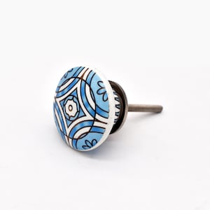 May include: A round ceramic cabinet knob featuring a light blue and white geometric pattern with dark brown outlines. The knob has a smooth, glossy finish and is attached to a silver-colored metal bolt extending from the back for installation.