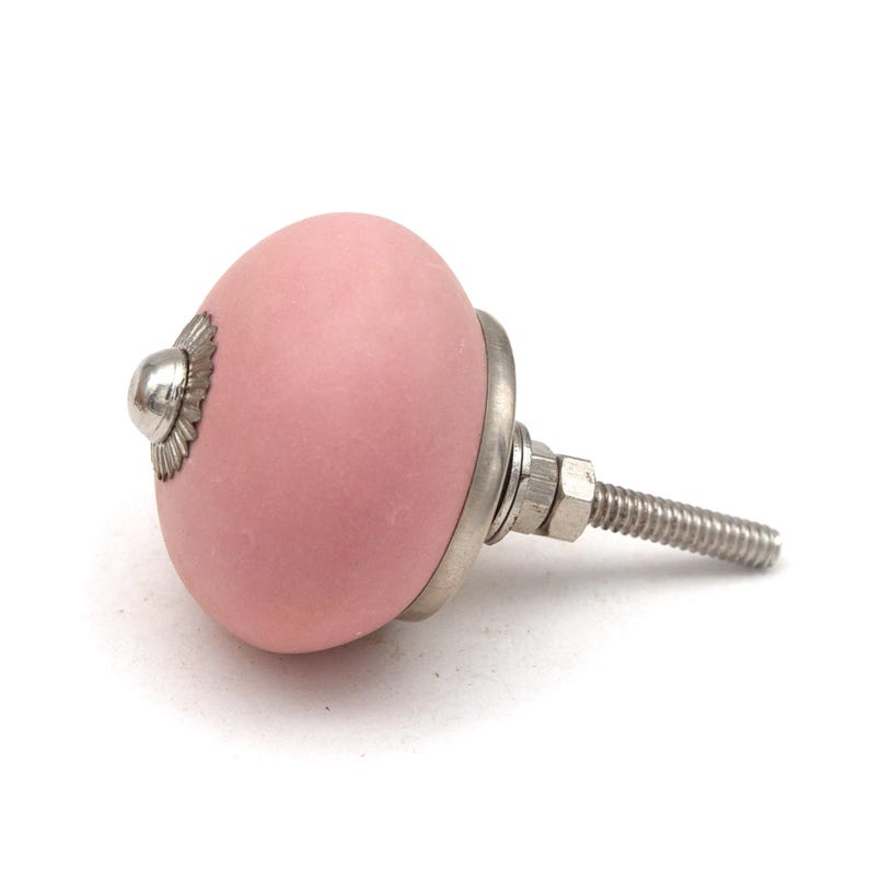May include: A pink ceramic cabinet knob with a silver metal base and threaded bolt. The knob has a rounded shape and a matte finish. The metal base has a decorative, scalloped edge.