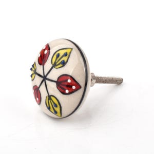 Peut inclure: Un bouton de meuble rond en céramique avec une base crème ornée d'un motif peint à la main de feuilles rouges et jaunes disposées en cercle. Les feuilles sont rehaussées de petits points blancs et bleus. Un boulon métallique dépasse à l'arrière.