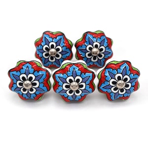 Puede incluir: Cinco tiradores decorativos de cerámica para armarios. Cada tirador tiene forma de flor con base blanca, diseño floral rojo, azul y verde, y centro metálico plateado. Los tiradores están dispuestos sobre un fondo blanco.