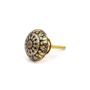 May include: A decorative cabinet knob with a black and gold mandala design. The knob has a round shape with a brass screw. The design features geometric and floral patterns.