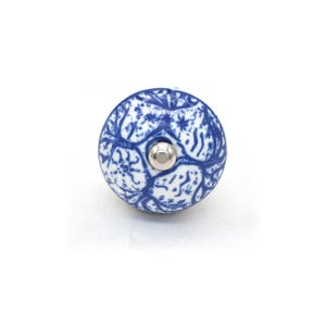 May include: A round, blue and white ceramic cabinet knob with a floral design. The knob has a silver-coloured metal screw. The design is a classic, decorative element for furniture.