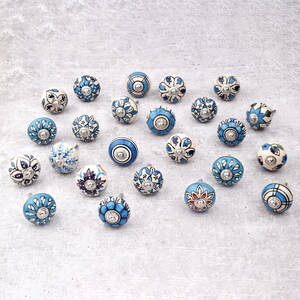 Assorted hand-painted ceramic knobs in blue, black and white with mandala and floral motifs for cupboard handles and kitchen decor.