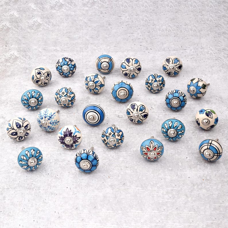 Assorted hand-painted ceramic knobs in blue, black and white with mandala and floral motifs for cupboard handles and kitchen decor.