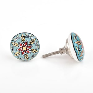Può includere: Due pomelli decorativi in ceramica per mobili. I pomelli presentano uno sfondo azzurro con un motivo floreale rosso, giallo e verde. I pomelli hanno una base e una vite in metallo argentato.