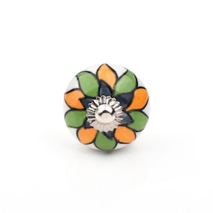 Può includere: Pomello decorativo per mobili in ceramica con un motivo floreale. Il pomello presenta una base bianca con disegni a forma di petali verdi, arancioni e blu scuro. Una vite in metallo color argento è attaccata sul davanti.