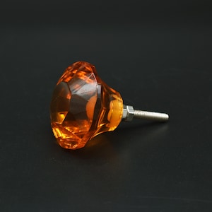 Op de afbeelding: Een gefacete oranje glazen kastknop met een zilveren schroef.