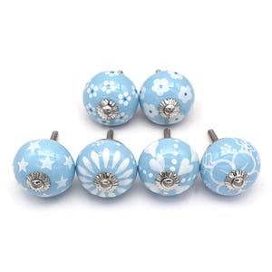 Hand-painted sky-blue ceramic knobs with assorted white designs (stars, flowers, stripes) for cabinets and drawers.