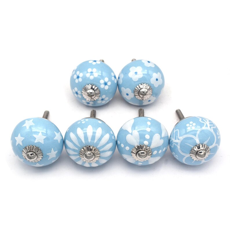 Hand-painted sky-blue ceramic knobs with assorted white designs (stars, flowers, stripes) for cabinets and drawers.