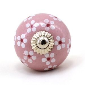 Könnte beinhalten: Rosafarbener Keramik-Knopf mit einem weißen und roten Blumenmuster. Der Knopf hat eine silberne Metallbasis.