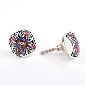 Può includere: Due pomelli per armadi in ceramica bianca con un motivo floreale rosso, blu e giallo. I pomelli hanno una forma quadrata con una vite metallica per l'installazione. Ferramenta decorativa per mobili.