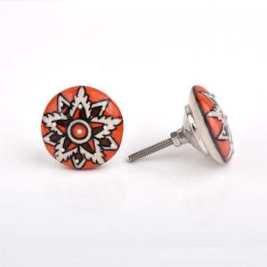 May include: Two ceramic cabinet knobs with a floral design. The knobs are orange with a black and white floral pattern. The hardware is silver-colored metal.