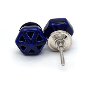 Könnte beinhalten: Zwei blaue Keramik-Schrankknöpfe mit geometrischem Design. Die Knöpfe haben eine silberne Metallbasis und eine Schraube.