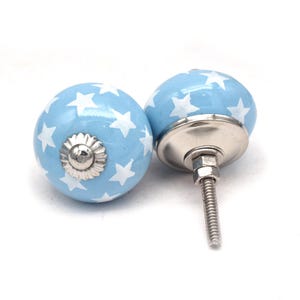 Op de afbeelding: Twee lichtblauwe keramische kastknoppen met witte sterren. De knoppen hebben een zilveren metalen basis en een schroef.