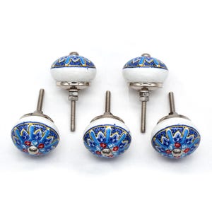 May include: Five ceramic cabinet knobs with a white base and intricate blue and red floral patterns. The knobs have a rounded shape and are mounted on silver-toned metal hardware. These decorative knobs are ideal for adding a touch of elegance to furniture.