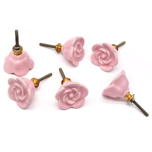 May include: Pink ceramic rose-shaped cabinet knobs with brass fittings. The knobs are arranged in different orientations, highlighting their design. These decorative knobs are perfect for adding floral elegance to furniture.