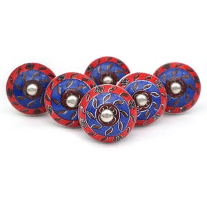 Könnte beinhalten: Sechs rote und blaue Keramik-Schrankknöpfe mit Blumenmuster. Die Knöpfe haben eine silberne Metallmitte.