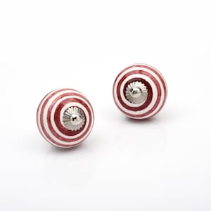 May include: Two round ceramic knobs featuring a spiral pattern of alternating dark red and white stripes. Each knob has a metallic silver-coloured centre piece with a scalloped edge, providing a decorative accent to the spherical surface design.