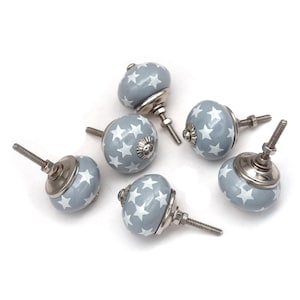 Könnte beinhalten: Sechs graue Keramik-Knöpfe mit weißen Sternenmustern und silbernen Metallsockeln.