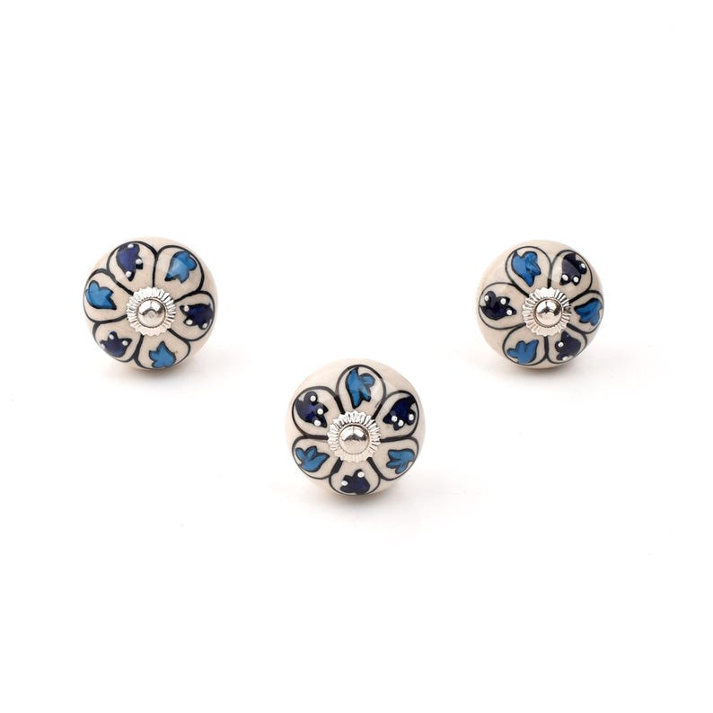 Assorted hand-painted ceramic knobs in blue, black and white with mandala and floral motifs for cupboard handles and kitchen decor.