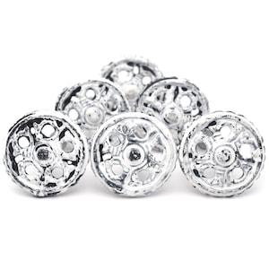 May include: A collection of six decorative cabinet knobs. Each knob is round with an openwork design, painted white with black accents. The knobs are made of metal and are suitable for furniture or home decor projects.