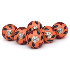 May include: Six orange ceramic cabinet knobs with a floral design in black and red. The knobs have a silver metal center.