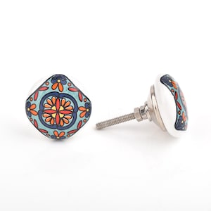 Può includere: Due pomelli decorativi in ceramica per mobili. Ogni pomello presenta una base bianca con un colorato motivo floreale nei toni del blu, arancione e rosso. I pomelli hanno una forma quadrata con una vite metallica per l'installazione.