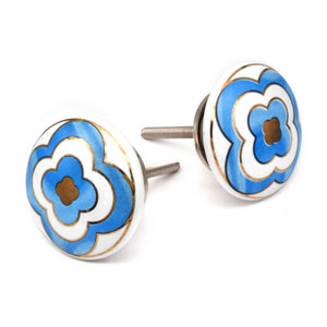 Może przedstawiać: Dwa ceramiczne gałki do szafek w kolorze niebieskim i białym z pozłacanym wykończeniem i wzorem kwiatowym. Gałki mają srebrną śrubę.