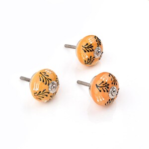 hand-painted ceramic round knobs in yellow-orange with black floral leaves for dresser knobs and cabinet pulls.