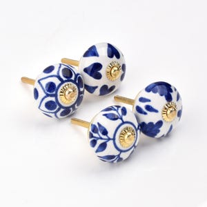 May include: Four white ceramic cabinet knobs with blue floral and heart patterns. Each knob has a gold-colored base and a threaded brass screw for installation. The knobs are arranged on a white surface.