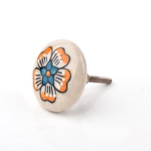May include: A ceramic cabinet knob with a floral design. The knob is off-white with a flower in shades of orange, blue, and black. The knob has a metal screw for attachment. Ideal for adding a decorative touch to furniture.