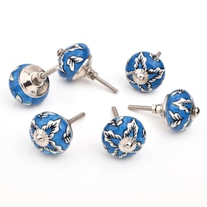 May include: Six blue and white ceramic cabinet knobs with silver fittings. The knobs are round with a floral design in white on a blue base. They are arranged on a white surface.