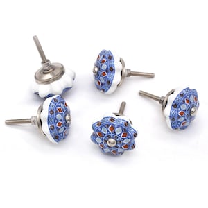 Op de afbeelding: Een verzameling van vijf decoratieve keramische kastknoppen. Elke knop heeft een witte, geschulpte rand en een blauw, rood en zilver geometrisch patroon. De knoppen hebben zilverkleurige metalen hardware voor installatie.
