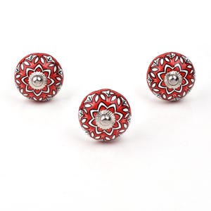 Red ceramic knobs with hand-painted white floral and mandala designs; assorted cabinet knobs for furniture and home décor.