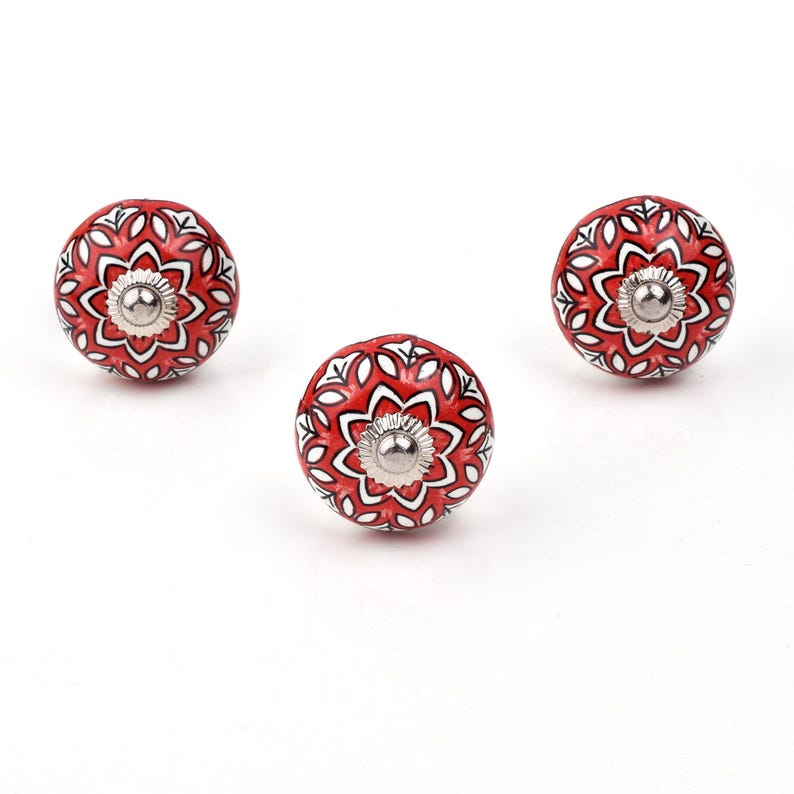 Red ceramic knobs with hand-painted white floral and mandala designs; assorted cabinet knobs for furniture and home décor.
