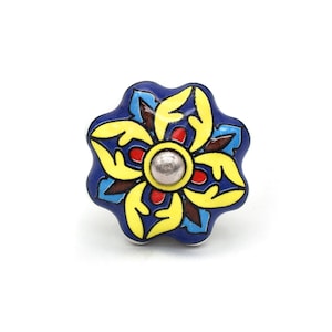 Puede incluir: Un tirador de cerámica para armario con diseño floral. El tirador presenta una base azul oscuro con detalles amarillos, rojos y marrones. El centro tiene una tapa de metal plateado. El tirador mide unos 5 cm de diámetro.