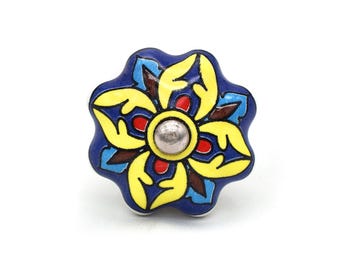 Op de afbeelding: Een keramische kastknop met een bloemmotief. De knop heeft een donkerblauwe basis met gele, rode en bruine accenten. Het midden heeft een zilverkleurige metalen dop. De knop heeft een diameter van ongeveer 5 cm.