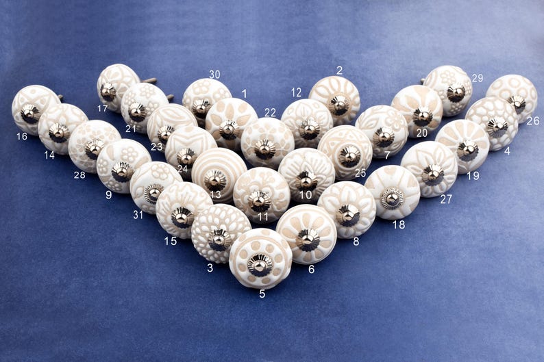 collection of white ceramic drawer knobs with intricate floral patterns and silver accents. The knobs are arranged in a basket lined with peach-colored fabric.