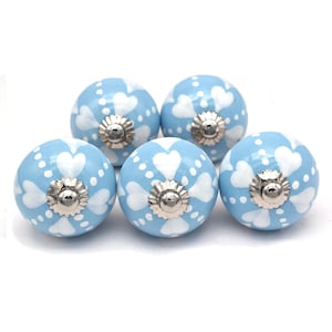 Könnte beinhalten: Fünf hellblaue Keramik-Schrankknöpfe mit weißen Herz- und Punktmustern. Jeder Knopf hat eine silberfarbene Metallbasis. Diese dekorativen Knöpfe sind ideal, um Möbeln oder Schränken einen Hauch von Charme zu verleihen.