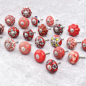 Red ceramic knobs with hand-painted white floral and mandala designs; assorted cabinet knobs for furniture and home décor.