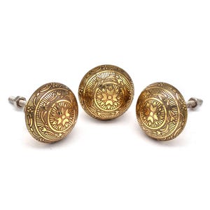 Könnte beinhalten: Drei goldfarbene Metall-Schrankknöpfe mit filigranen Blumenmustern. Jeder Knopf hat eine Schraube zum Befestigen an einer Schranktür.