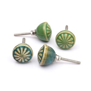 May include: A collection of twelve decorative cabinet knobs in various colours and patterns. Each knob features a round or oval shape with a metal bolt extending from the back. The designs include floral, geometric, and solid textures in shades of green, blue, orange, purple, white, and grey.