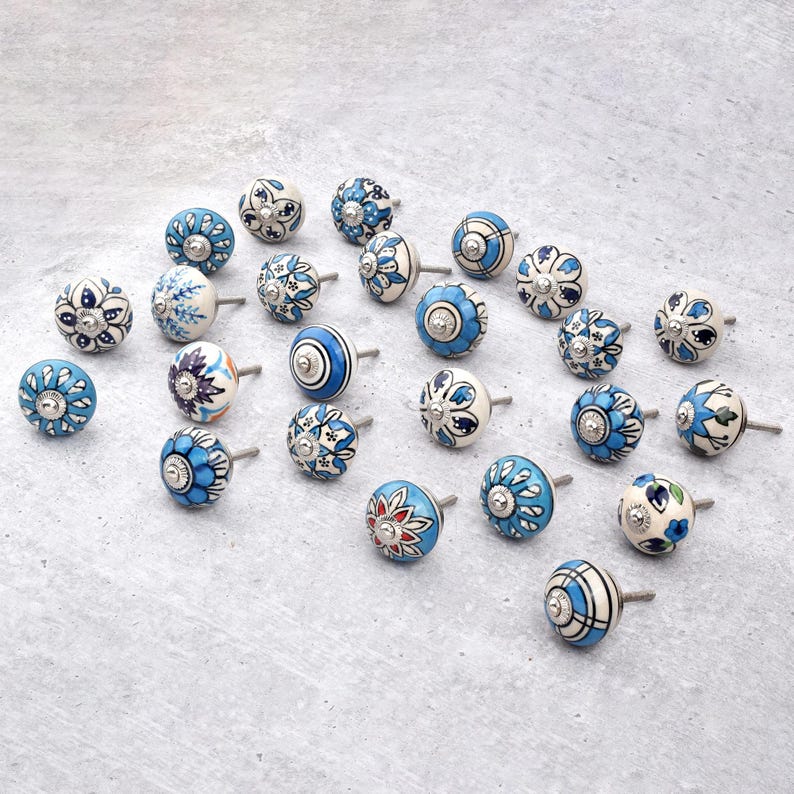 Assorted hand-painted ceramic knobs in blue, black and white with mandala and floral motifs for cupboard handles and kitchen decor.