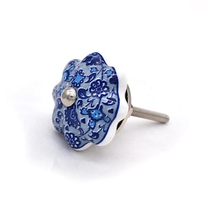 May include: A decorative cabinet knob with a floral design. The knob is a light blue and white color with a silver screw. The floral pattern is in shades of blue.